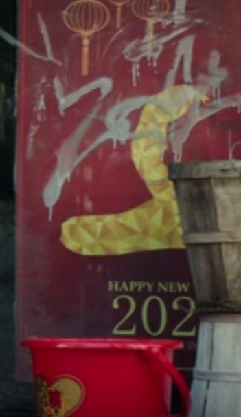 A poster on the wall says "Happy New" then the rest is hidden behind a box, and the year is twenty twenty-something, but we only see the first three numbers, so it's like "Happy New Redacted, 2 0 2 Redacted".